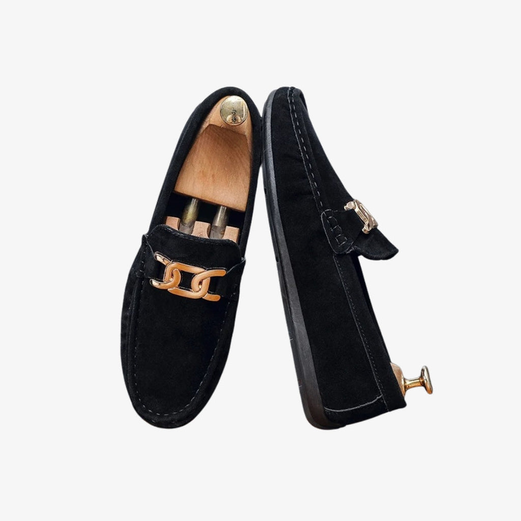 Loafer aus schwarzem Kunstwildleder für Herren, elegant und modern, mit einer goldenen Metallschnalle auf dem Spann. Ihr raffiniertes Design hebt sichtbare Nähte hervor, die dem Ganzen einen Hauch von Charakter verleihen. Die schwarze Sohle rundet ihr schlichtes, schickes Aussehen ab.