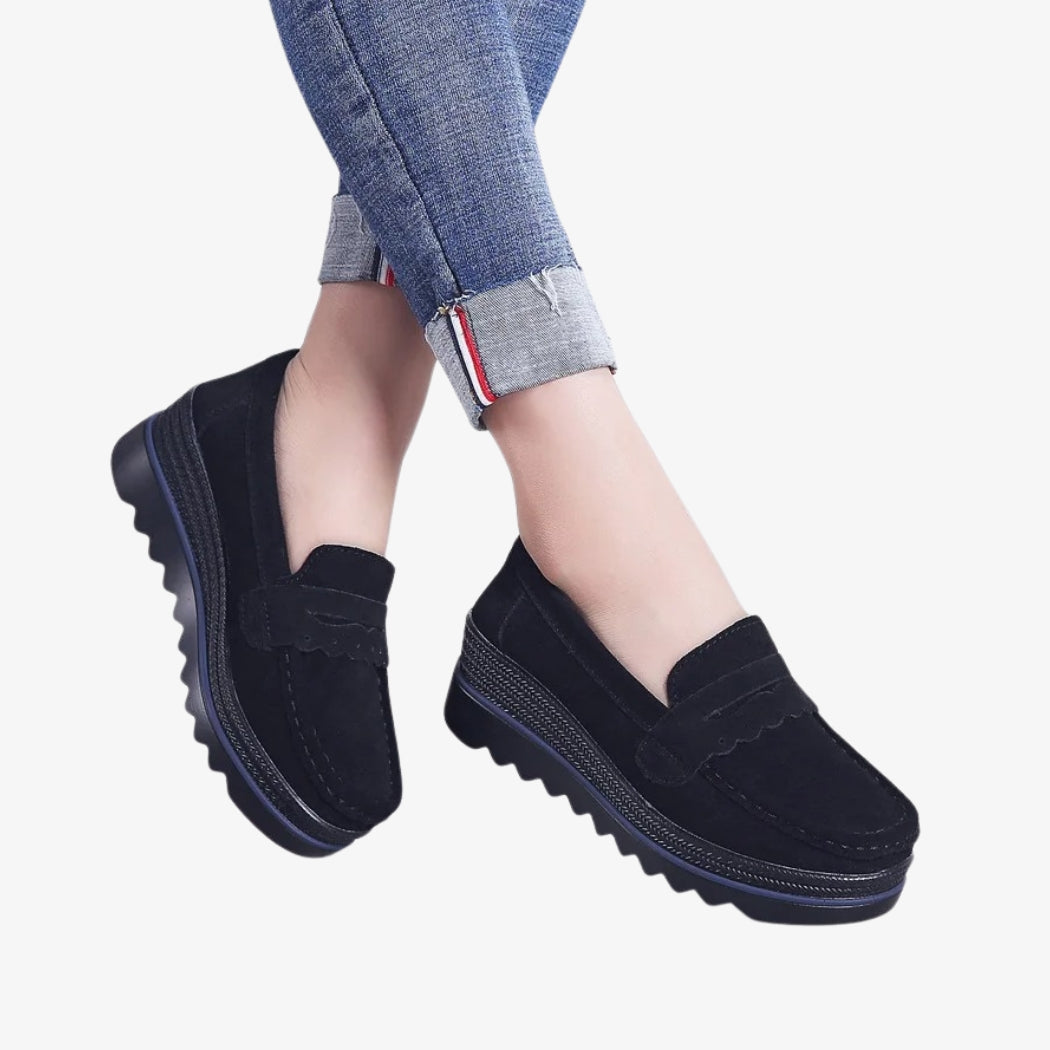 Loafer für Damen aus schwarzem Wildleder, elegant und bequem, mit profilierten Keilsohlen für mehr Stabilität. Das Design bietet dekorative Details auf der Oberseite und eine sichtbare Naht, perfekt für einen modernen, lässigen Stil.