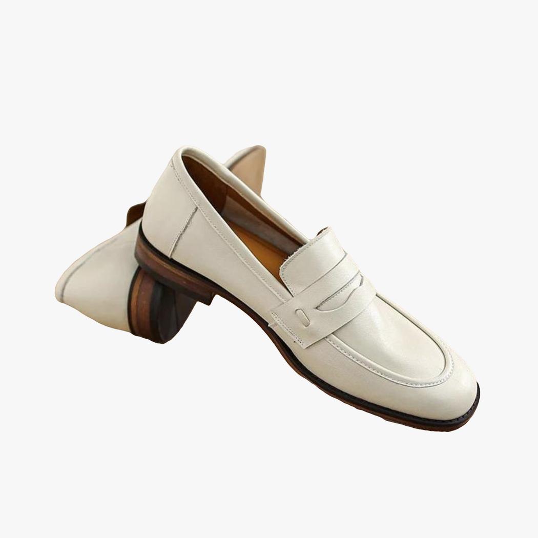 Ein Paar beige Loafer mit braunen Sohlen aus Echtleder liegt auf einem Holzstamm