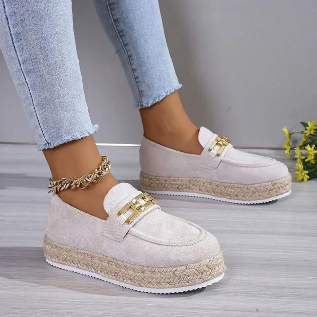 Die Füße einer Frau in Jeans, die beige Keilabsatz-Mokassins aus synthetischem Wildleder trägt