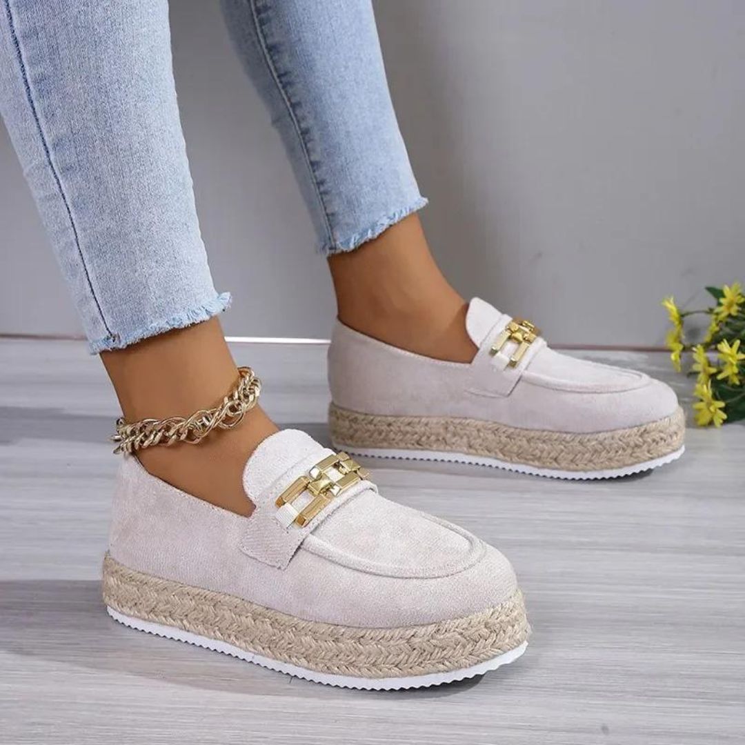 Die Füße einer Frau in Jeans, die beige Keilabsatz-Mokassins aus synthetischem Wildleder trägt