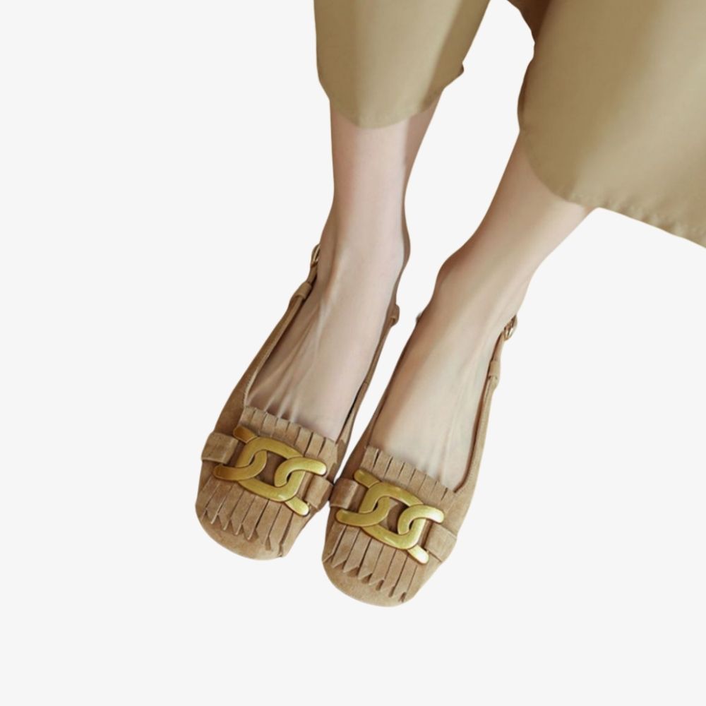 Beige Mokassins mit Fransen und goldenem Zierelement auf dem Spann, von einer Frau getragen