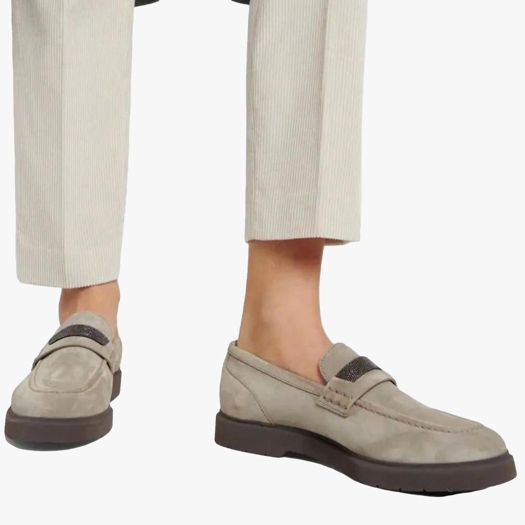 Zu sehen sind die Füße einer Frau, die eine beige Anzughose und graue Loafer aus echtem Wildleder für Damen trägt