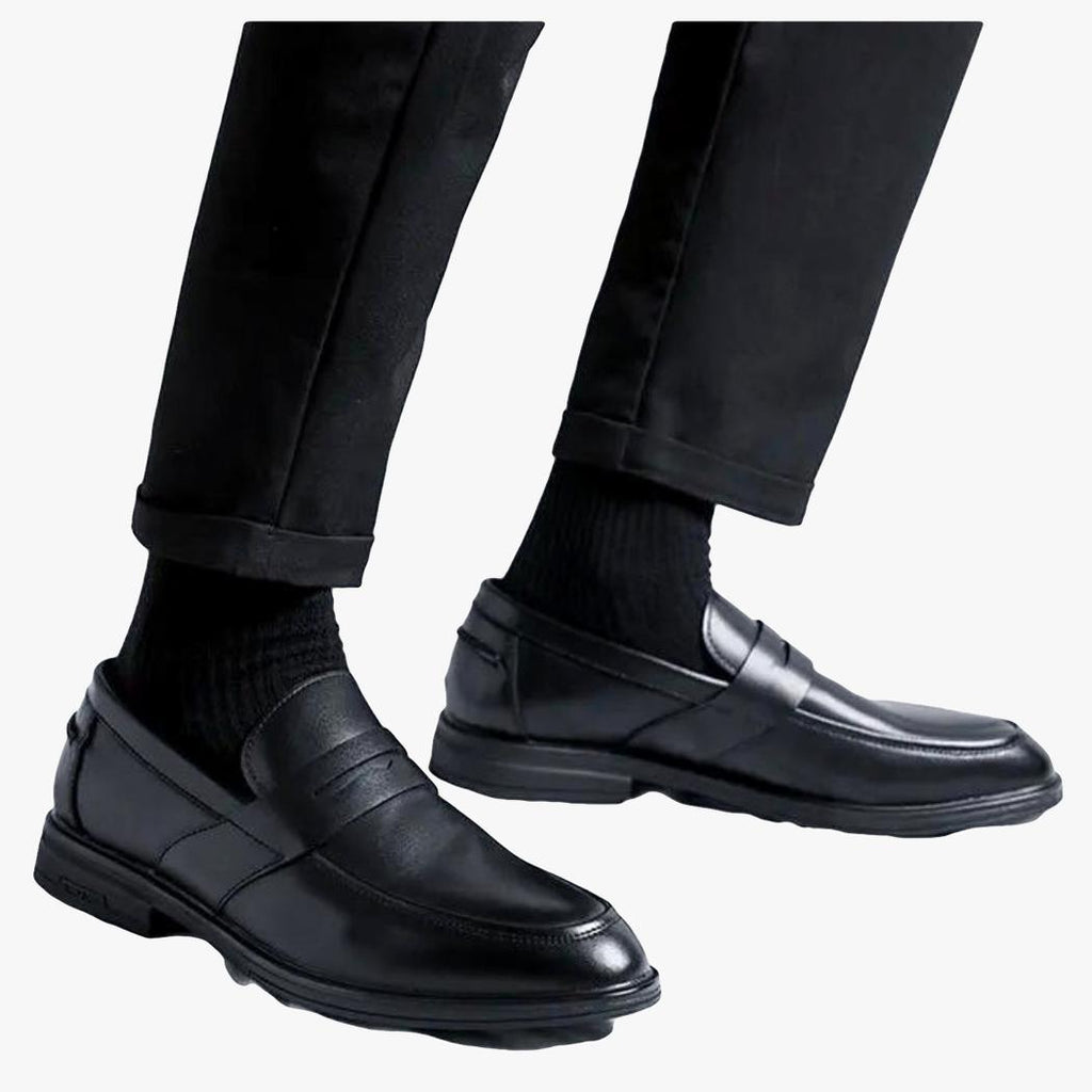 Auf hellem Hintergrund sind die Unterschenkel eines Mannes zu sehen, der eine schwarze Hose und klassische schwarze Loafer aus Kunstleder für Herren trägt