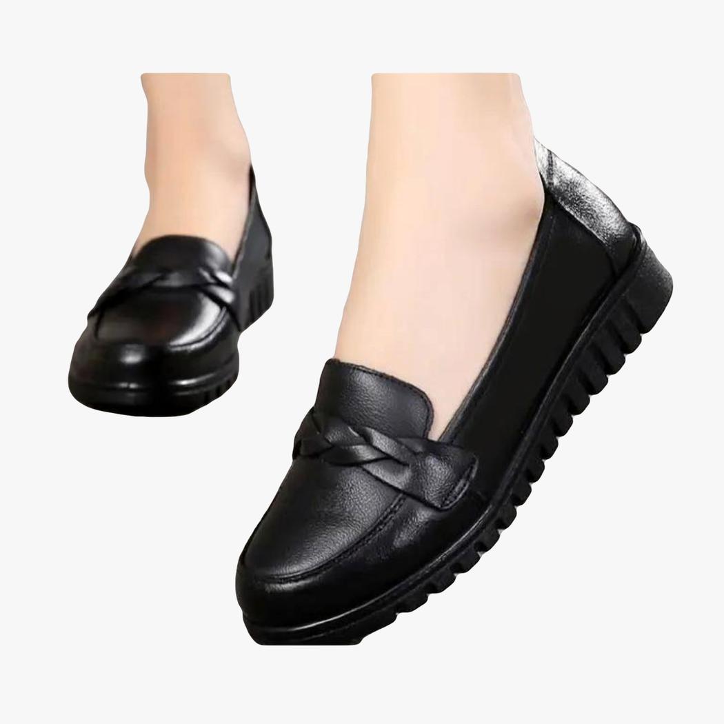Ein Paar schwarze Loafer, getragen von einer Frau, man sieht nur ihre Füße