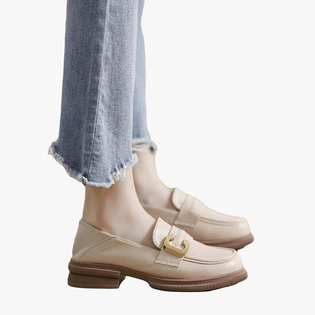 Die Füße einer Frau in Jeans, die weiche beige Mokassins aus Kunstleder trägt