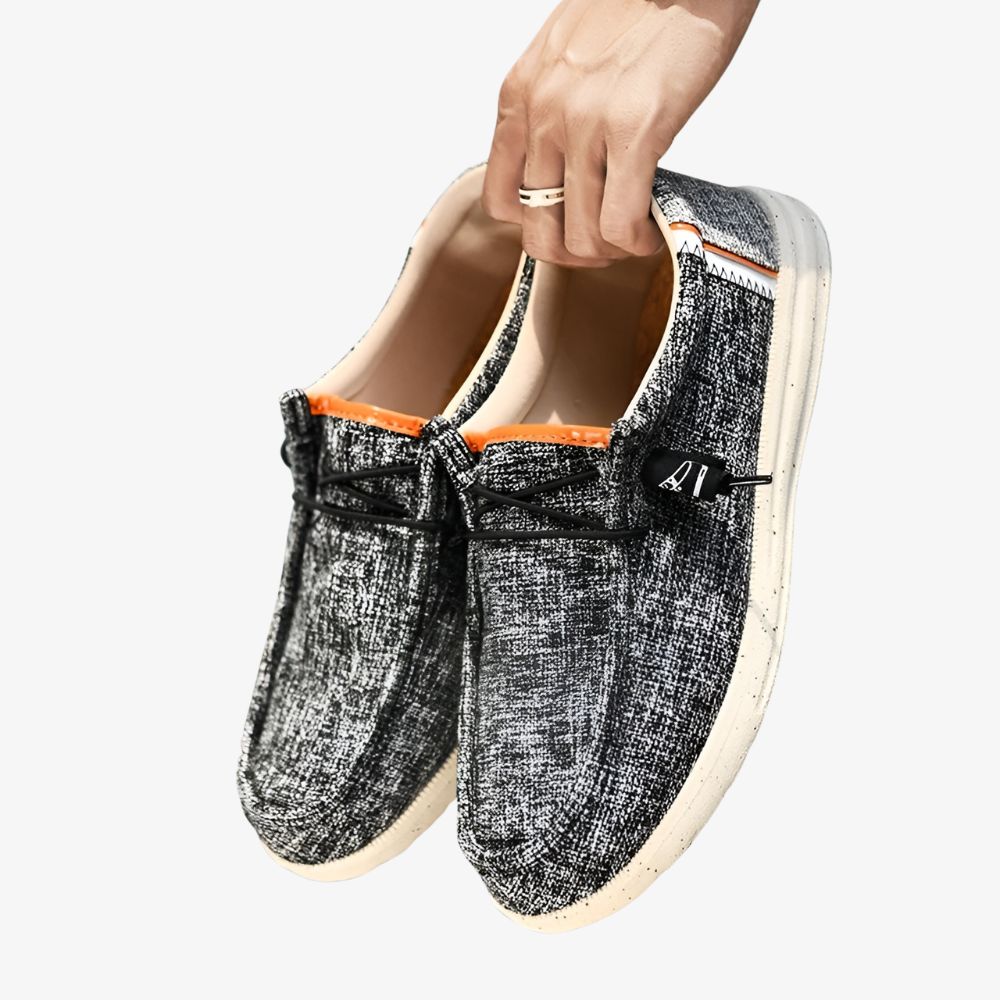 Paar graue Canvas-Loafer für Herren mit kleinen schwarzen Flecken und weißer Sohle.