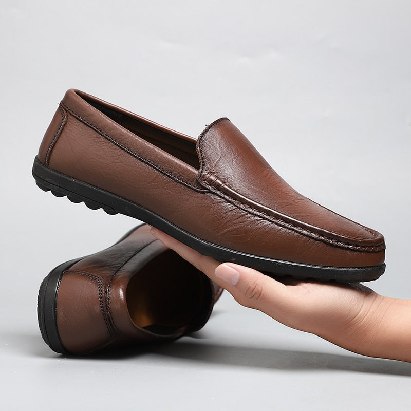 brauner Mokassin aus Leder in der Hand eines Mannes mit dem anderen Paar Schuhe dahinter