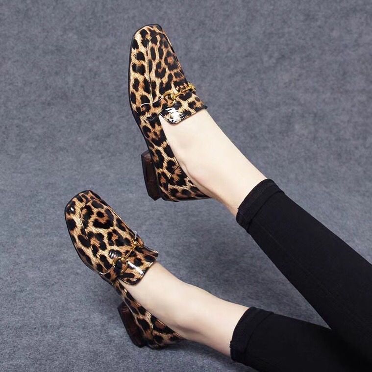 Auf grauem Hintergrund, Beinpaar mit schwarzen Leggings und glänzenden Mokassins mit quadratischen Absätzen mit Leopardenmuster