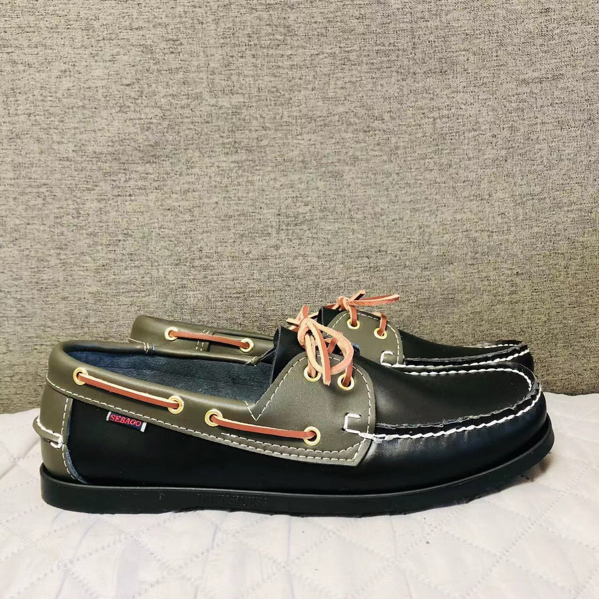 Ein Paar schwarze und khakifarbene Bootsmokassins auf einem weißen Boden im Profil