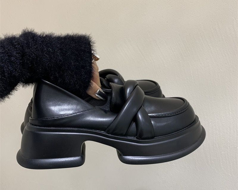 Schwarze Plateau-Mokassins aus Kunstleder für Frauen mit beigem Hintergrund und einer Frau, die das Paar Schuhe hält