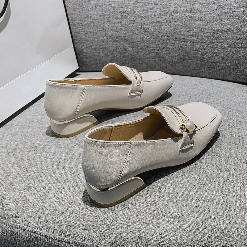 weißer PU-Mokassin mit kleinem Absatz, der auf einem grauen Sofa liegt