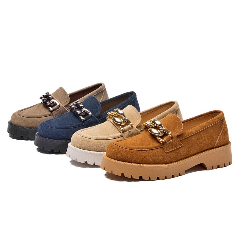 Vier Mokassins aus Wildleder in verschiedenen Farben, graublau, beige und braun mit dicker Sohle und großer goldener Zierschnalle, die auf einem weißen Hintergrund aufgereiht sind.