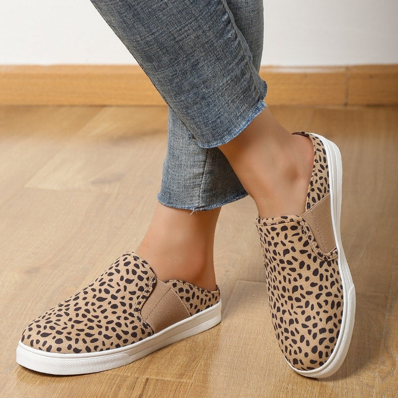 beinkleider in Jeans mit sichtbaren Knöcheln, die beigefarbene Mokassins mit Leopardenmuster und weißem Plateau auf einem beigen Parkettboden tragen.
