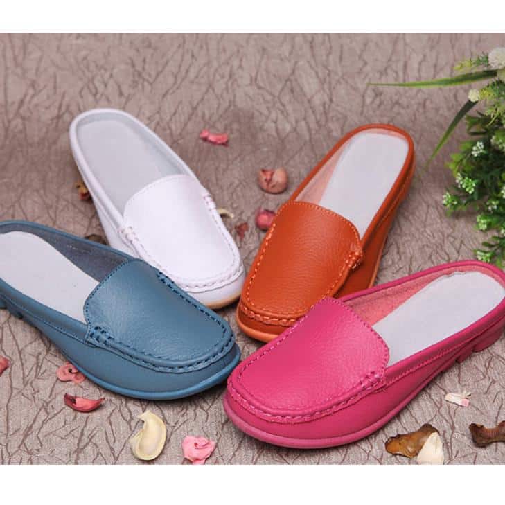 4 Mokassin-Pantoletten in Blau, Weiß, Orange und Rosa mit Steppnähten auf der Oberseite und weißen Einlegesohlen. Sie stehen auf einem beigen Boden mit rosa und beigen Blütenblättern rundherum