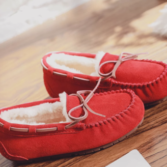 Foto von einem Paar gefütterter Wildledermokassins in verschiedenen Rottönen, die auf einem Holzmöbel liegen.