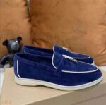 Blauer Mokassin aus Wildleder mit weißem Rand und einer harten Quaste auf der Vorderseite des Schuhs, der auf einem Schuhkarton steht