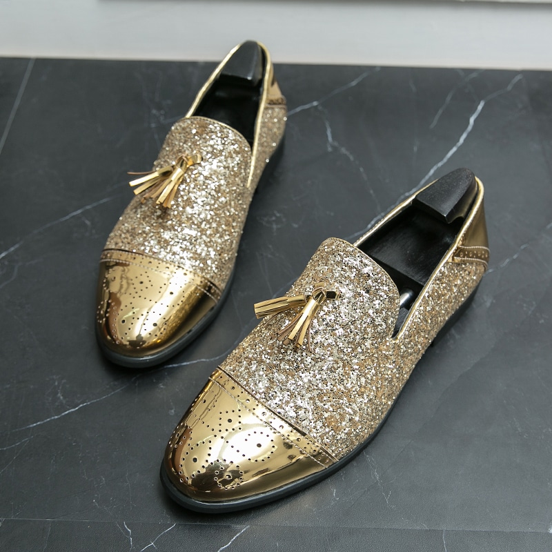 Auf einem grau marmorierten Boden, ein Paar Mokassins mit Quasten aus Lack und goldenen Pailletten mit schwarzen Schuhspannern an der Innenseite