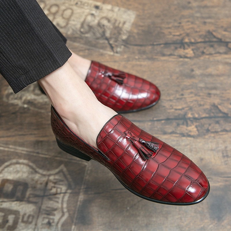 Füße tragen rote Mokassins mit Krokodilhaut-Effekt und einer Quaste auf der Oberseite des Schuhs