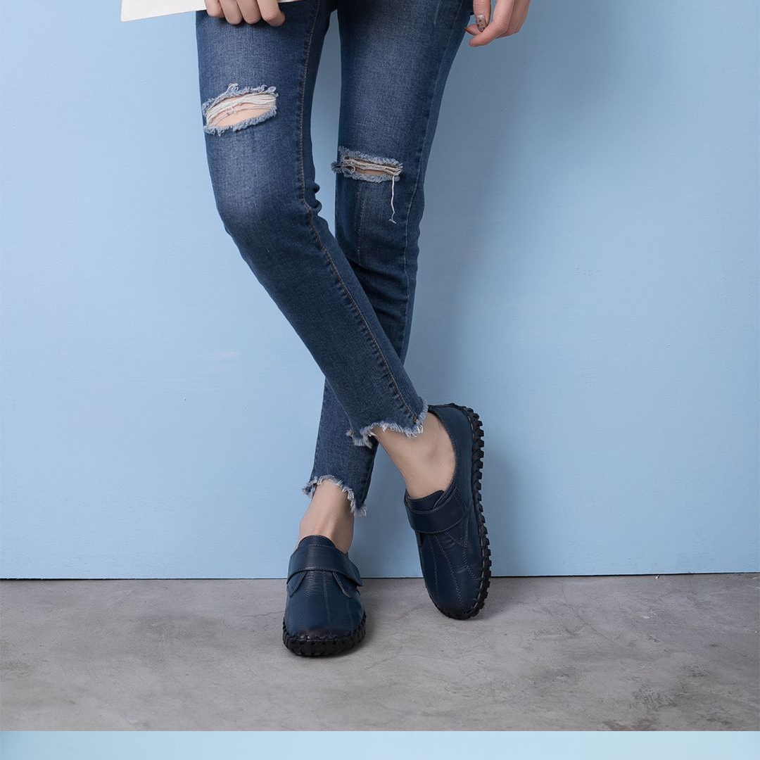 Beine einer Person, die mit gekreuzten Beinen steht und eine löchrige Jeans und blaue Schuhe trägt.