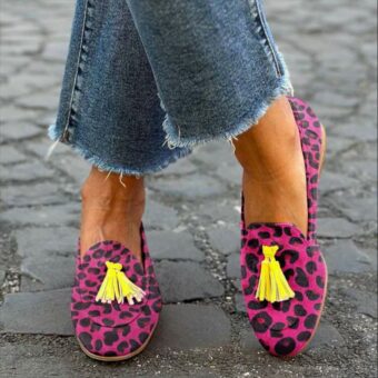 Frau steht mit gekreuzten Beinen auf der Straße und trägt Jeans und Mokassins mit Quasten mit rosafarbenem Leopardenmuster