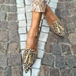 Frau auf der Straße mit gekreuzten Füßen, die spitze Mokassins mit goldenem Leopardenmuster trägt