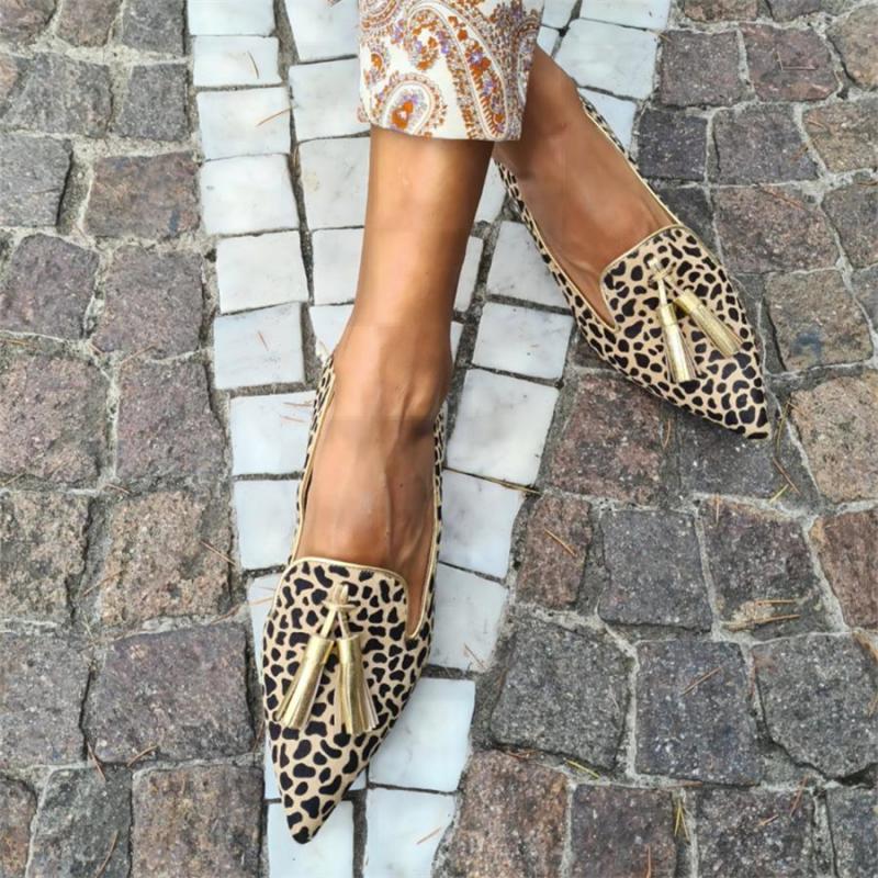 Frau auf der Straße mit gekreuzten Füßen, die spitze Mokassins mit goldenem Leopardenmuster trägt