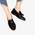Mocassins pour femme en cuir verni noir, élégants et brillants. Ces chaussures sont ornées de glands décoratifs sur le dessus, ajoutant une touche classique et sophistiquée. Leur design intemporel convient parfaitement pour un look chic et décontracté.